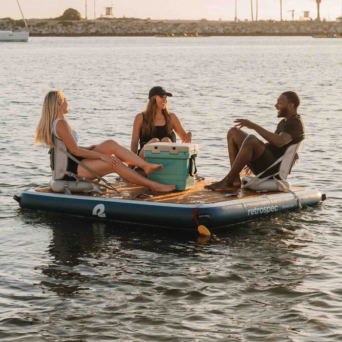 Three people sitting on inflatable seats attached to an inflatable platform in the water with a cooler between them.