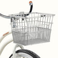 A silver wire basket mounted on a bicycle’s handlebars, paired with a white bike frame and black tire.