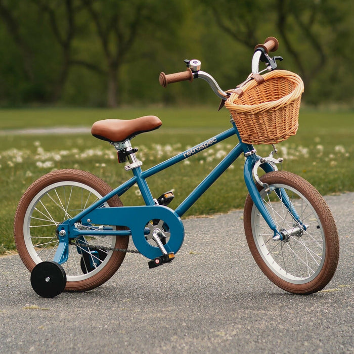 A blue Beaumont Mini 16" Kids' Bike with a wicker basket, brown handlebars, and training wheels parked on a pathway, surrounded by greenery.