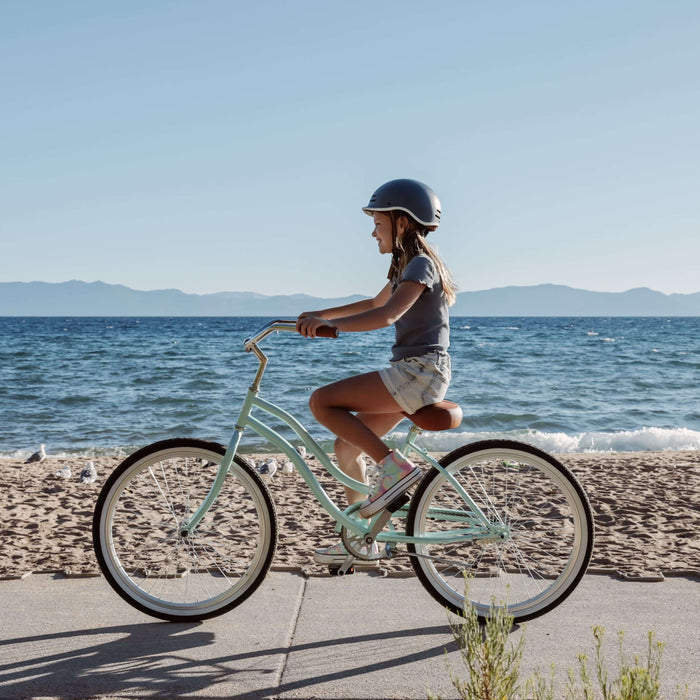 Person riding a light blue bicycle along a path by the beach.