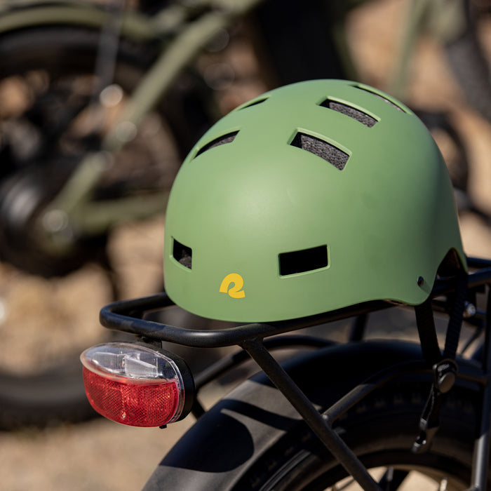 A green Dakota Bike & Skate Helmet with a small retrospec logo set on a bike rack with a blurred background.