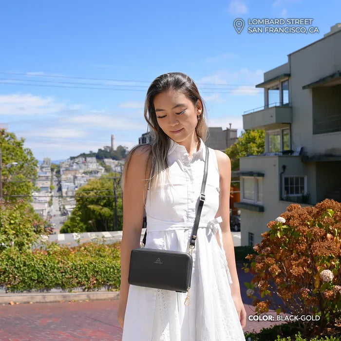 Woman in a white outfit with a Anti-theft Marina Grande Wallet in black/gold handbag standing outdoors in San Francisco.