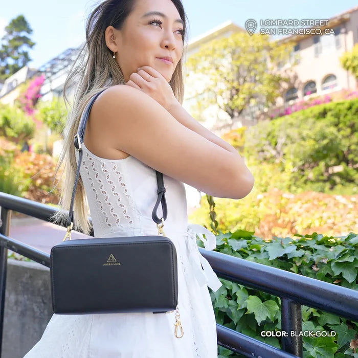 Woman in a white outfit with a Anti-theft Marina Grande Wallet in black/gold handbag standing outdoors in San Francisco.