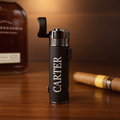 Black matte triple torch lighter with "CARTER" engraved vertically, silver-tone top, integrated punch and rest, displayed with cigar and whiskey bottle