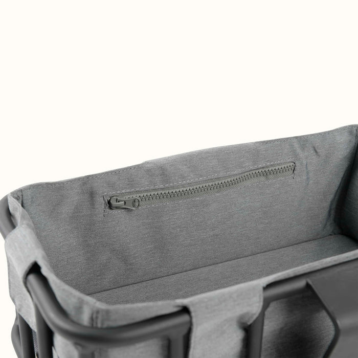 A close-up of a gray fabric basket liner with a zippered pocket and the metal basket's solid back frame.